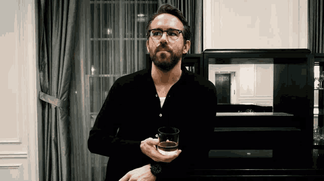 a man with glasses holds a glass of whiskey in his hand