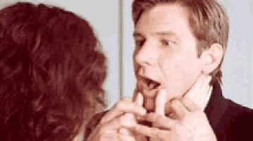 a woman is touching a man 's face with her hands while he looks at her .
