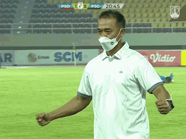 a man wearing a mask stands on a soccer field with a scoreboard behind him that says psg