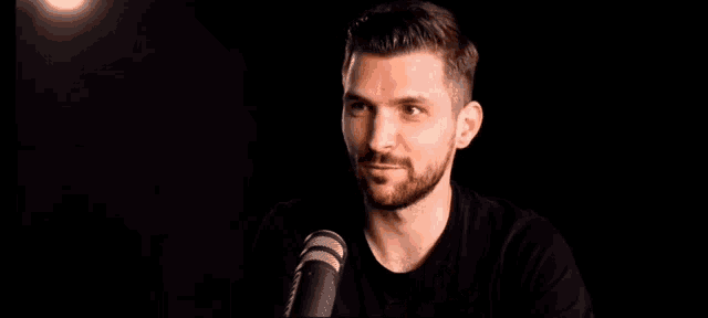 a man with a beard is speaking into a microphone with the words there has never been a better time to be alive .