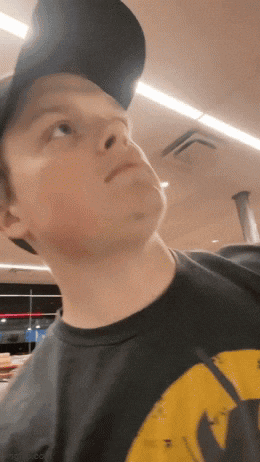 a young man wearing a hat and a black shirt with a yellow wu tang logo on it