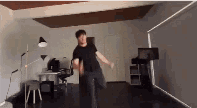 a man in a black shirt is dancing in a room with a desk and chairs .