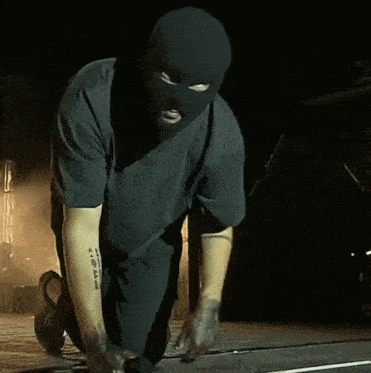 a man wearing a ski mask and a black shirt with a tattoo on his arm