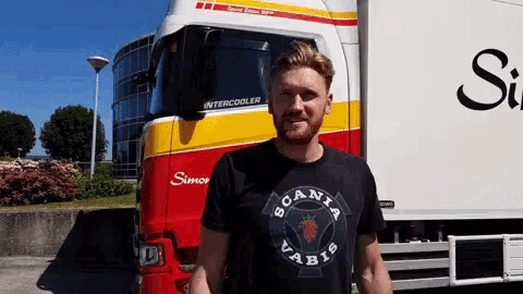 a man wearing a scania t-shirt stands in front of a semi truck