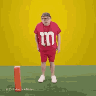 a man wearing a red m & ms shirt and shorts is dancing on a field .
