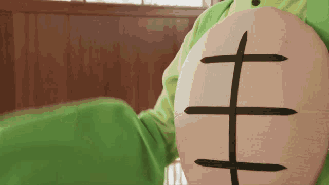 a person in a green shirt is holding a wooden shield with a black cross on it