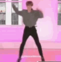 a man in a grey shirt and black pants is dancing in a pink room .