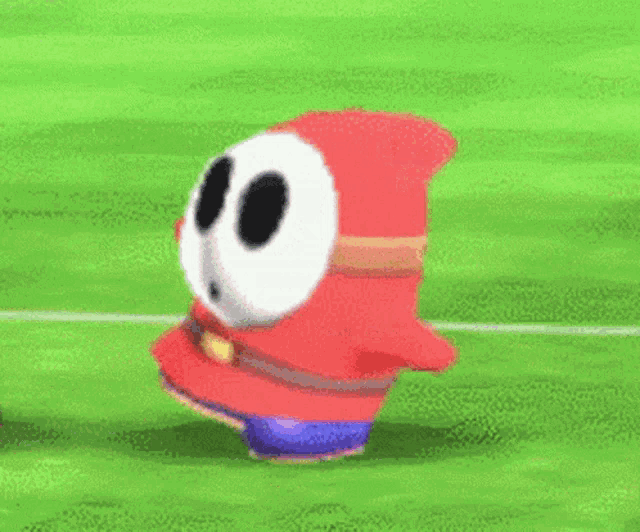 shy guy from super mario bros is jumping in the air on a green field .