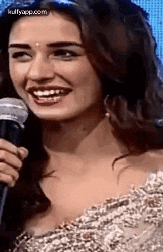 a woman is smiling while holding a microphone and looking at the camera .