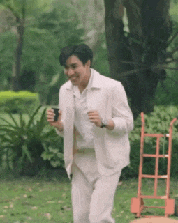 a man in a white suit is running in a park and holding a cup .