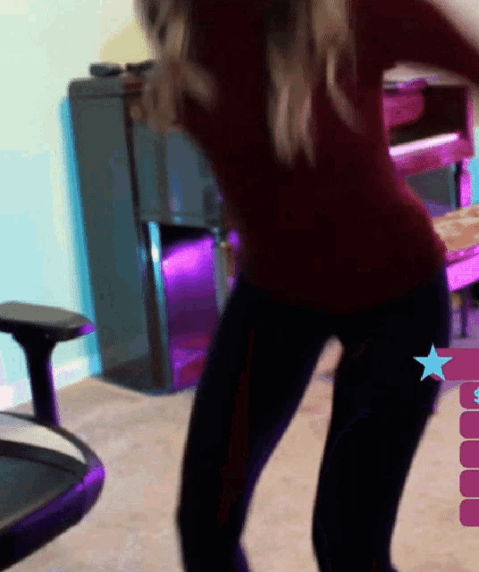 a woman in a red shirt and black pants is dancing in a room with purple lights