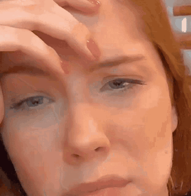 a close up of a woman 's face with her hands on her forehead .