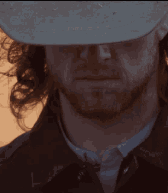 a man with long hair and a beard wearing a cowboy hat