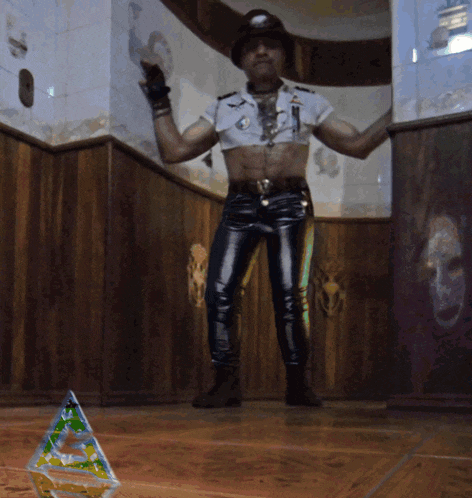 a man in a hat and leather pants stands in front of a green triangle