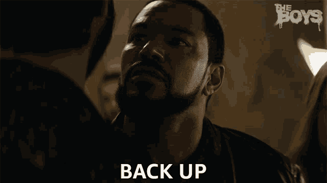 a man with a beard says " back up " in a dark room