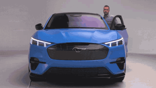a man stands next to a blue mustang with its doors open