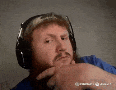 a man with a beard wearing headphones and a blue shirt is looking at the camera .