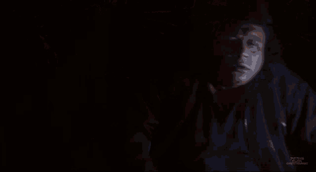 a man in a black jacket is standing in the dark looking at something .