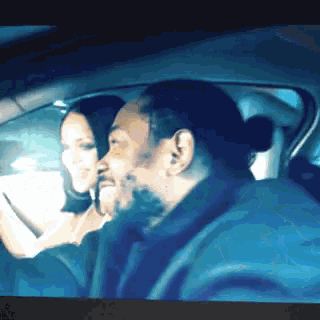a man with a ponytail is driving a car with a woman in the back seat