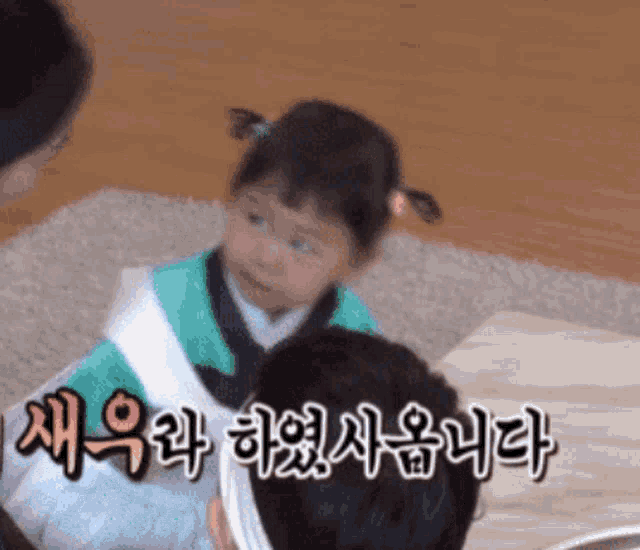 a little girl sitting on a man 's lap with korean writing on the bottom right