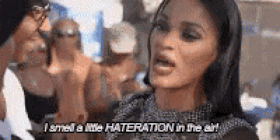 a woman is talking to a man in a crowd and says `` i smell a little hateration in the air '' .