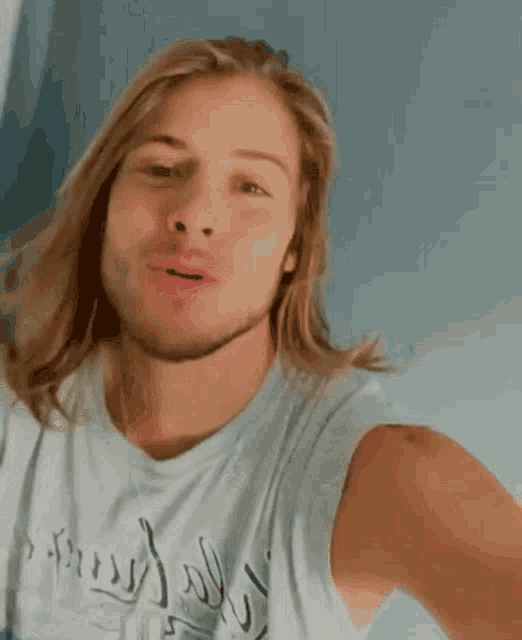 a man with long blonde hair and a beard is smiling and wearing a tank top that says ' inspired ' on it