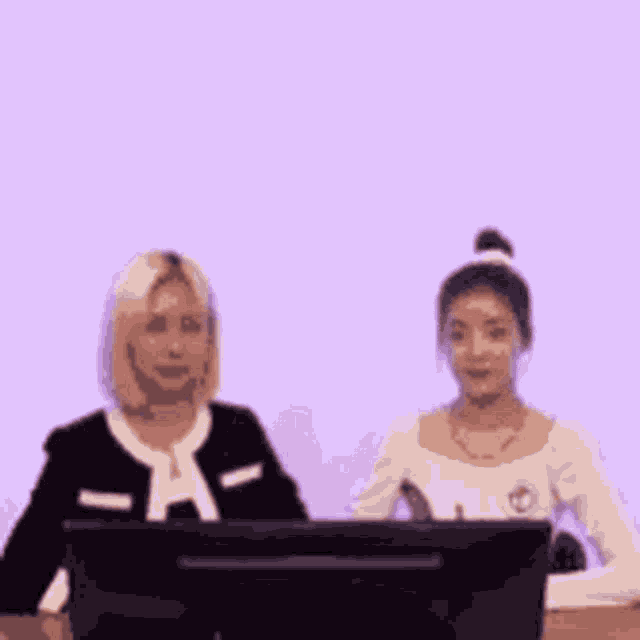 two women are sitting in front of a computer .
