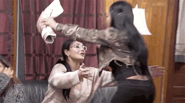 two women are fighting over a piece of paper in a living room while sitting on a couch .
