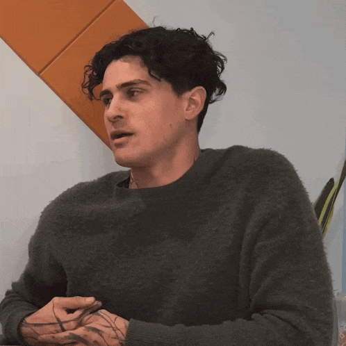a man with curly hair is wearing a sweater and has a tattoo on his arm
