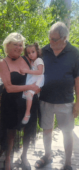 a woman in a black dress is holding a little girl while a man in a blue shirt stands behind her