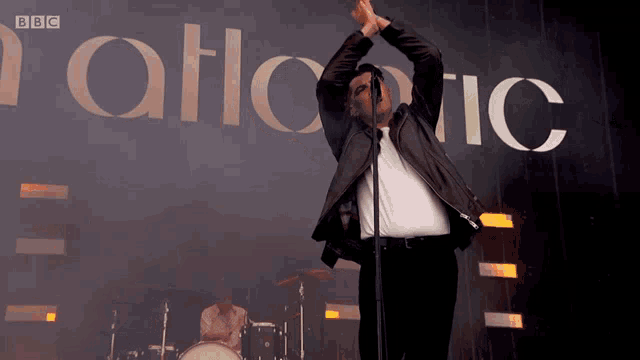 a man sings into a microphone in front of a sign that says bbc