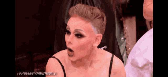 a woman with a shaved head is wearing a black bra and has her mouth open .