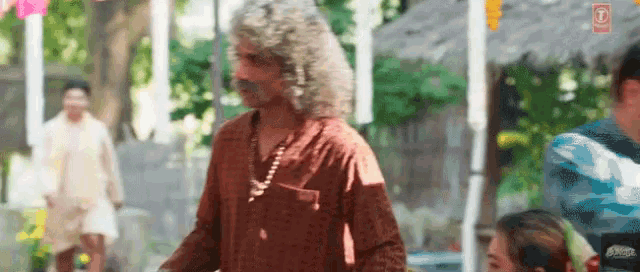 a man with long curly hair and a mustache is standing in front of a crowd of people .