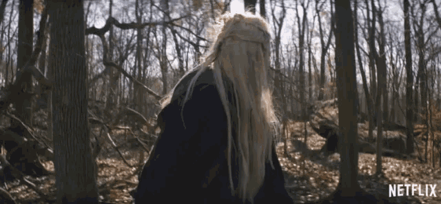 a woman with long blonde hair is walking through the woods with a netflix logo in the corner