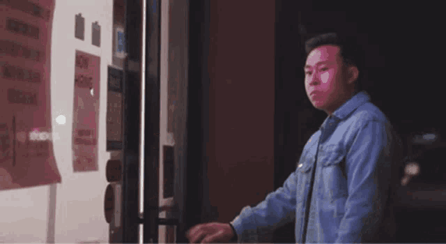 a man in a denim jacket is standing in front of a glass door with a sign on it