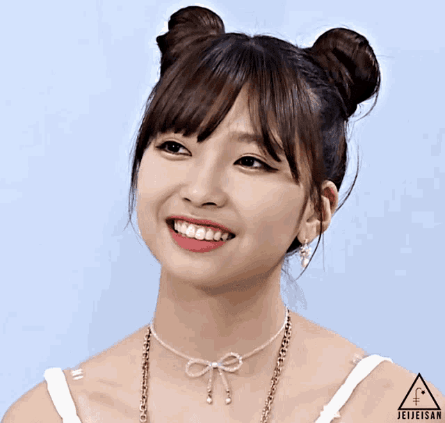 a girl with two buns on her head is smiling and wearing a necklace with a bow