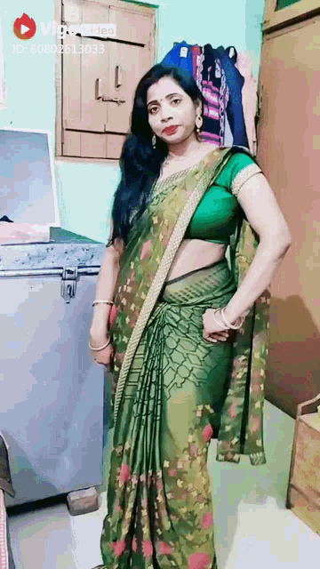 a woman in a green saree is standing in front of a refrigerator .