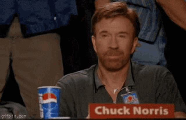 a man sitting at a table with a sign that says " chuck norris "