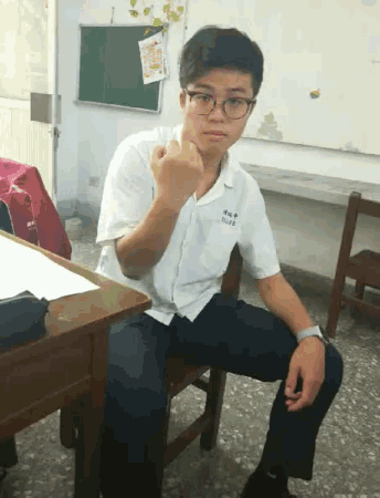 a young man wearing glasses and a white shirt with the number 48 on it sits at a desk