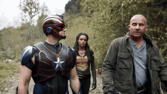 a man in a superhero costume is walking down a dirt road with two other people .