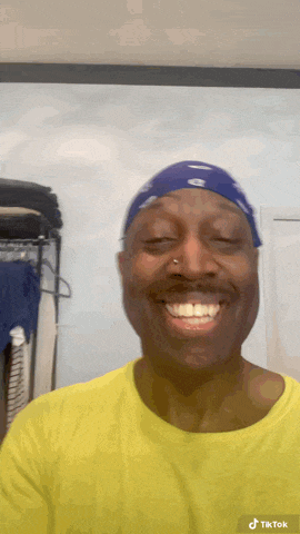 a man wearing a blue bandana and a yellow shirt is smiling .