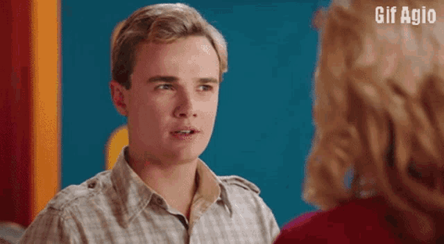 a man in a plaid shirt is talking to a woman with the words gif agio written above him