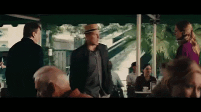 a man in a hat is standing in front of a group of people sitting at tables in a restaurant .