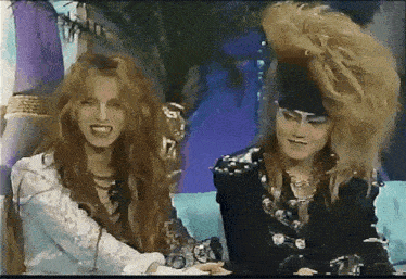 a man and a woman are sitting next to each other and one has a big hairdo