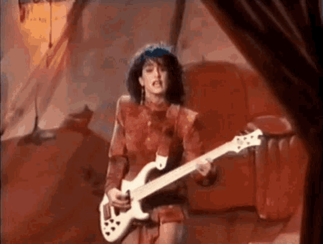 a woman in a red dress is playing a white electric guitar .