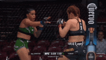 two women are fighting in a boxing ring with a bottle of corona in the background
