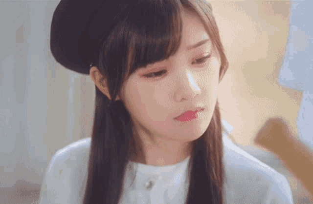 a young woman wearing a hat and a white shirt is looking down .