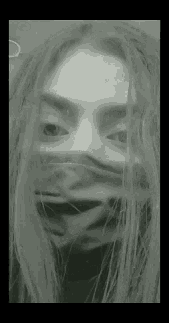 a black and white photo of a woman covering her face with a mask