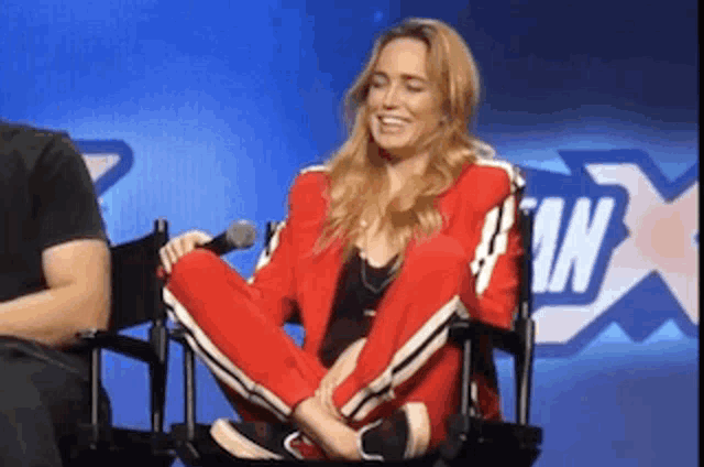 a woman in a red jacket is sitting in a chair with her legs crossed and smiling .