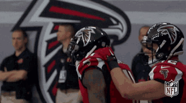 two atlanta falcons football players hugging in front of a nfl logo